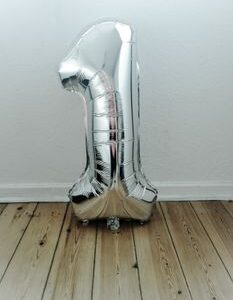 A large silver number one balloon against a white wall on a wooden floor, perfect for celebrations.