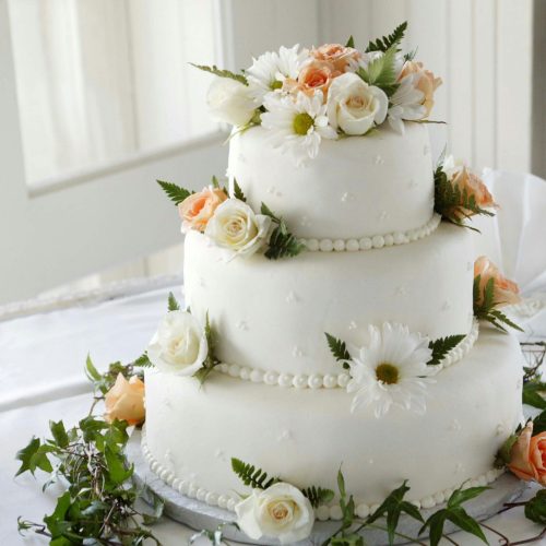 pexels-photo-1702373-1702373 Elegant white wedding cake adorned with fresh roses and daisies, perfect for a romantic celebration.